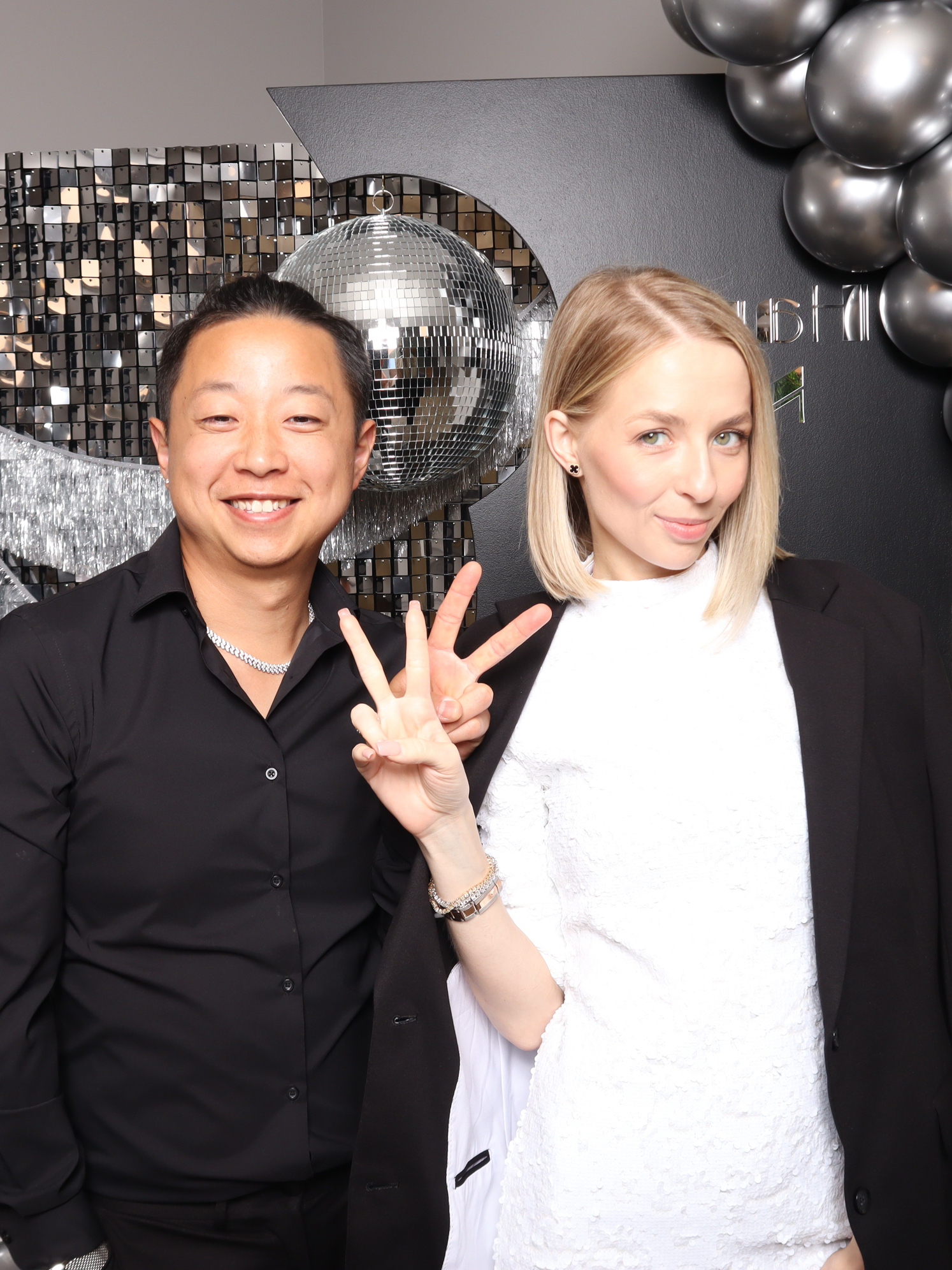 Couple posing beside a disco ball and silver sequin backdrop with black balloons