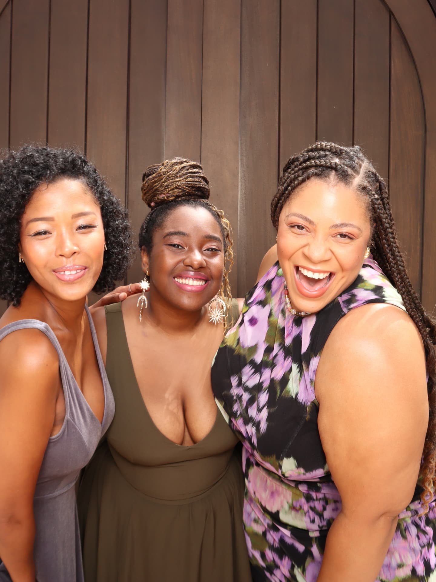 Three friends laughing together in front of a wood backdrop