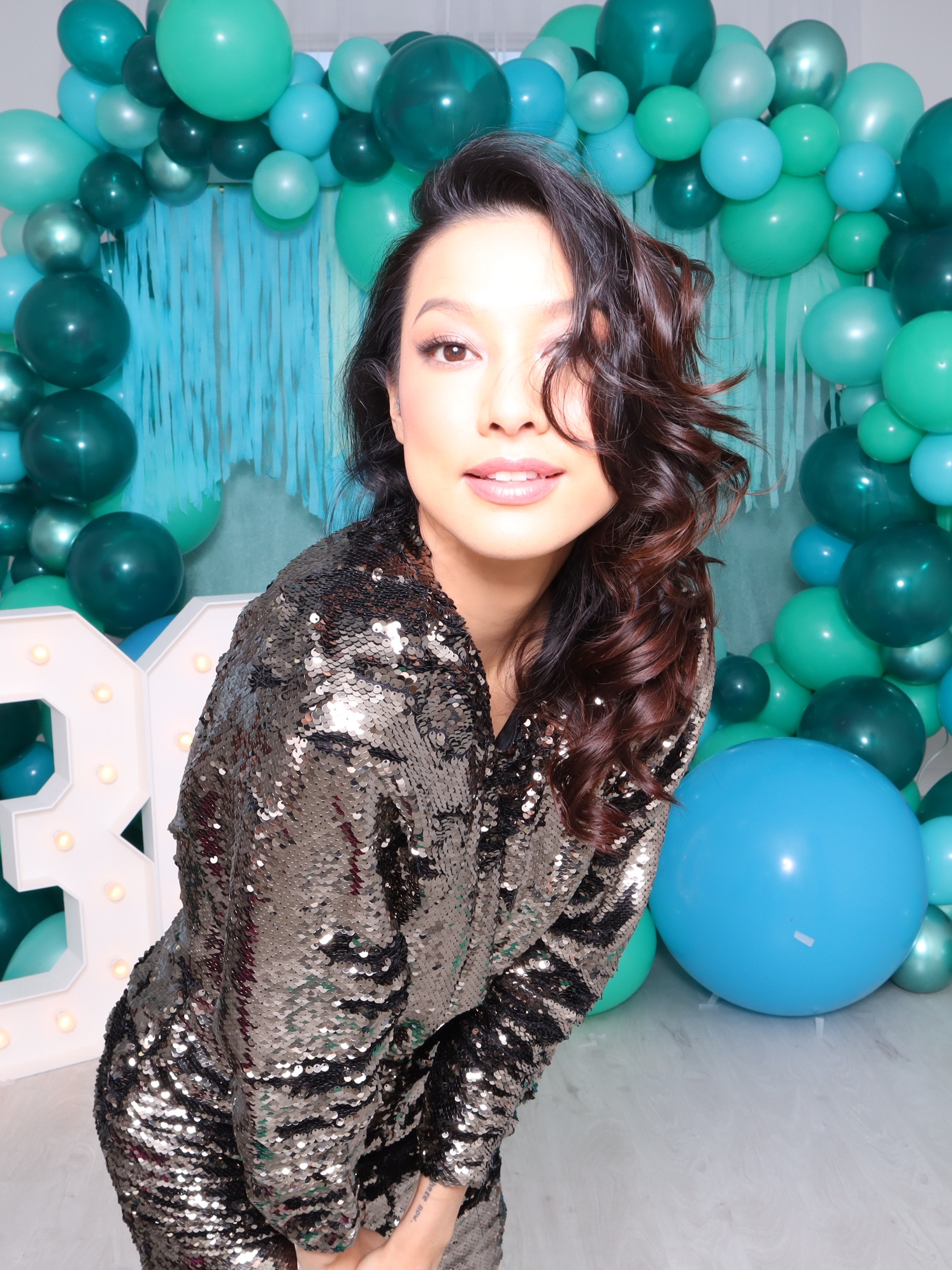 Guest in a sequin dress posing beside a teal balloon arch