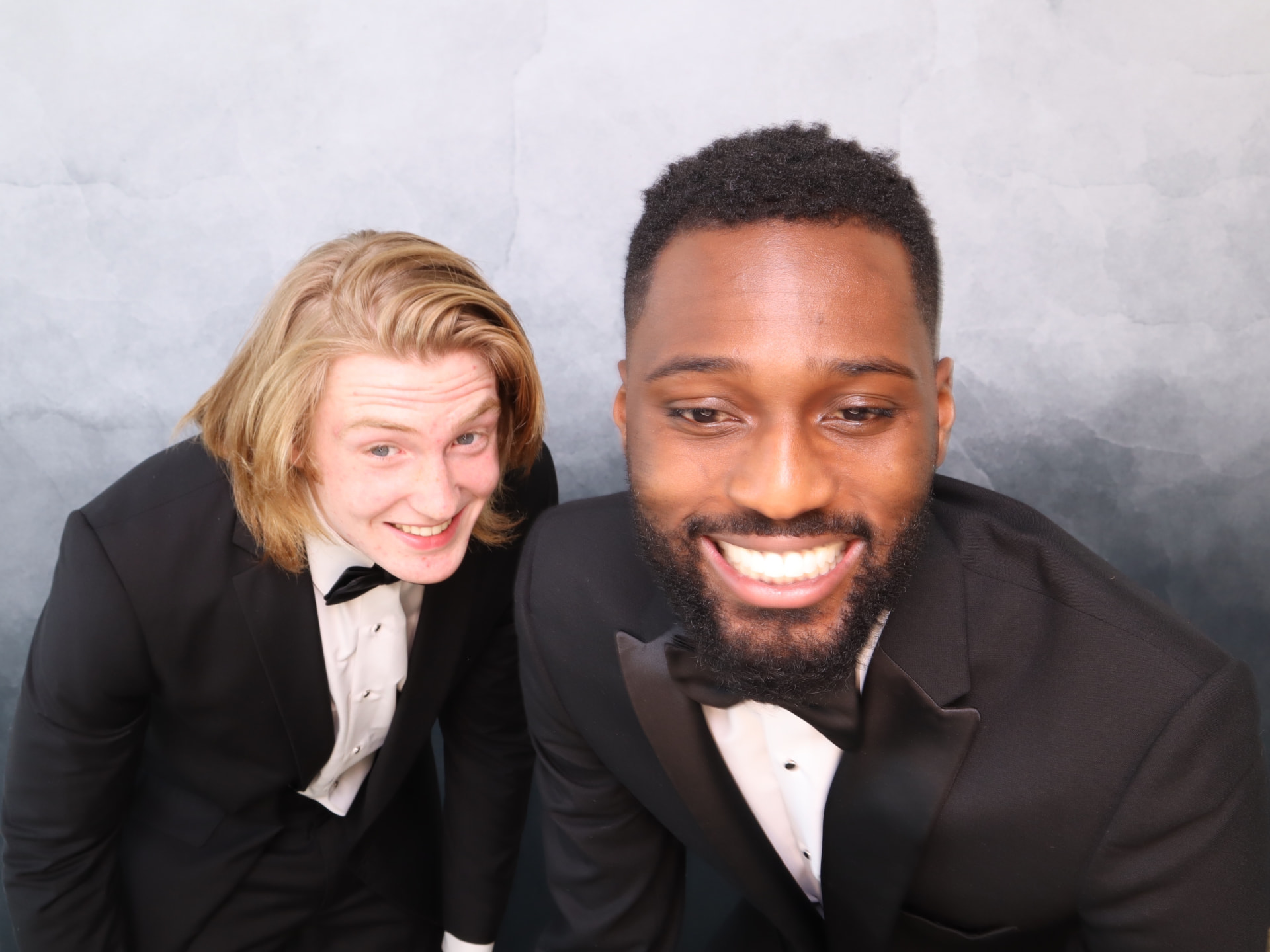 Two guests in tuxedos laughing in a studio photo booth