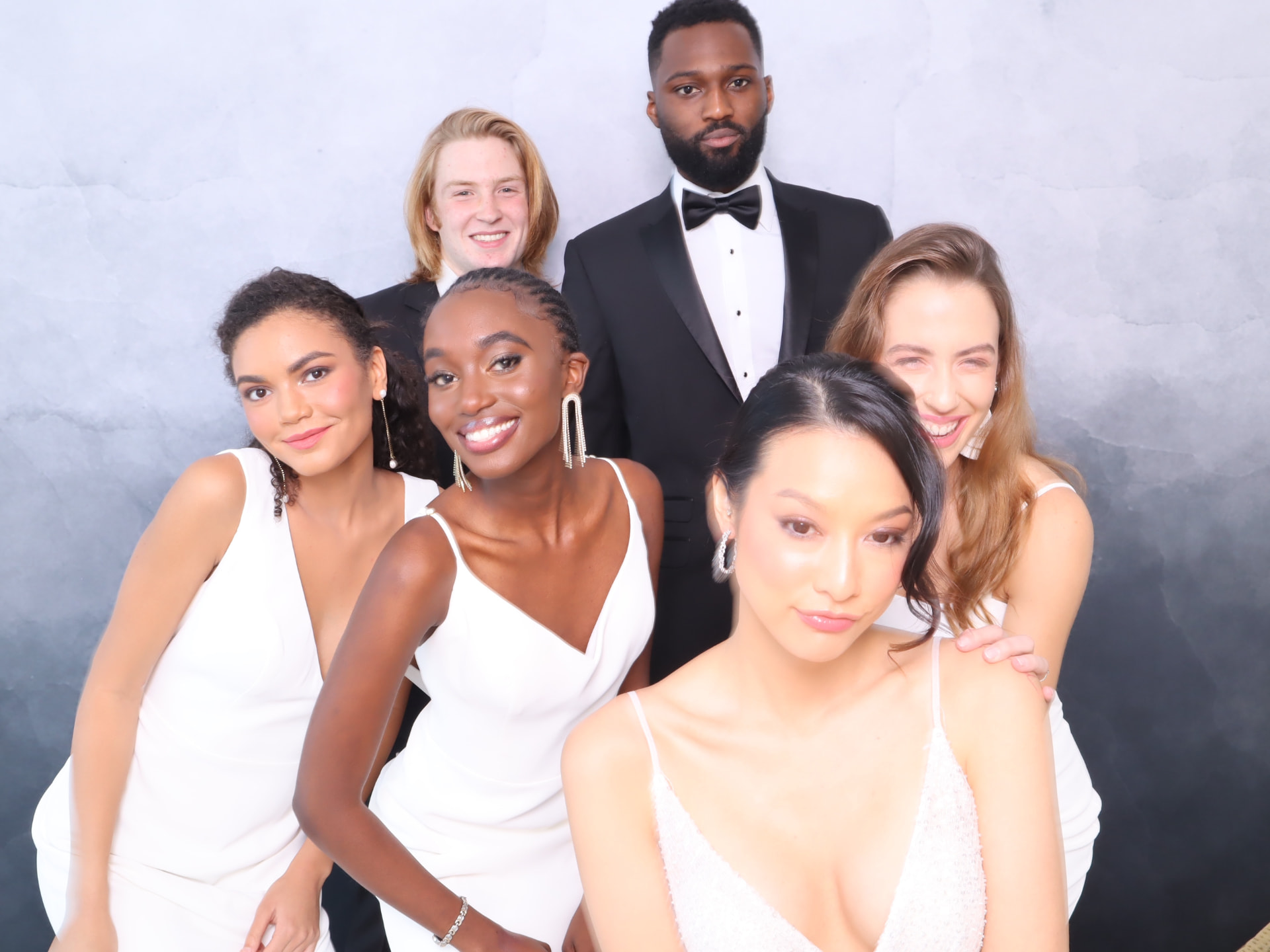 Guests in white gowns and tuxedos posing playfully in a studio photo booth